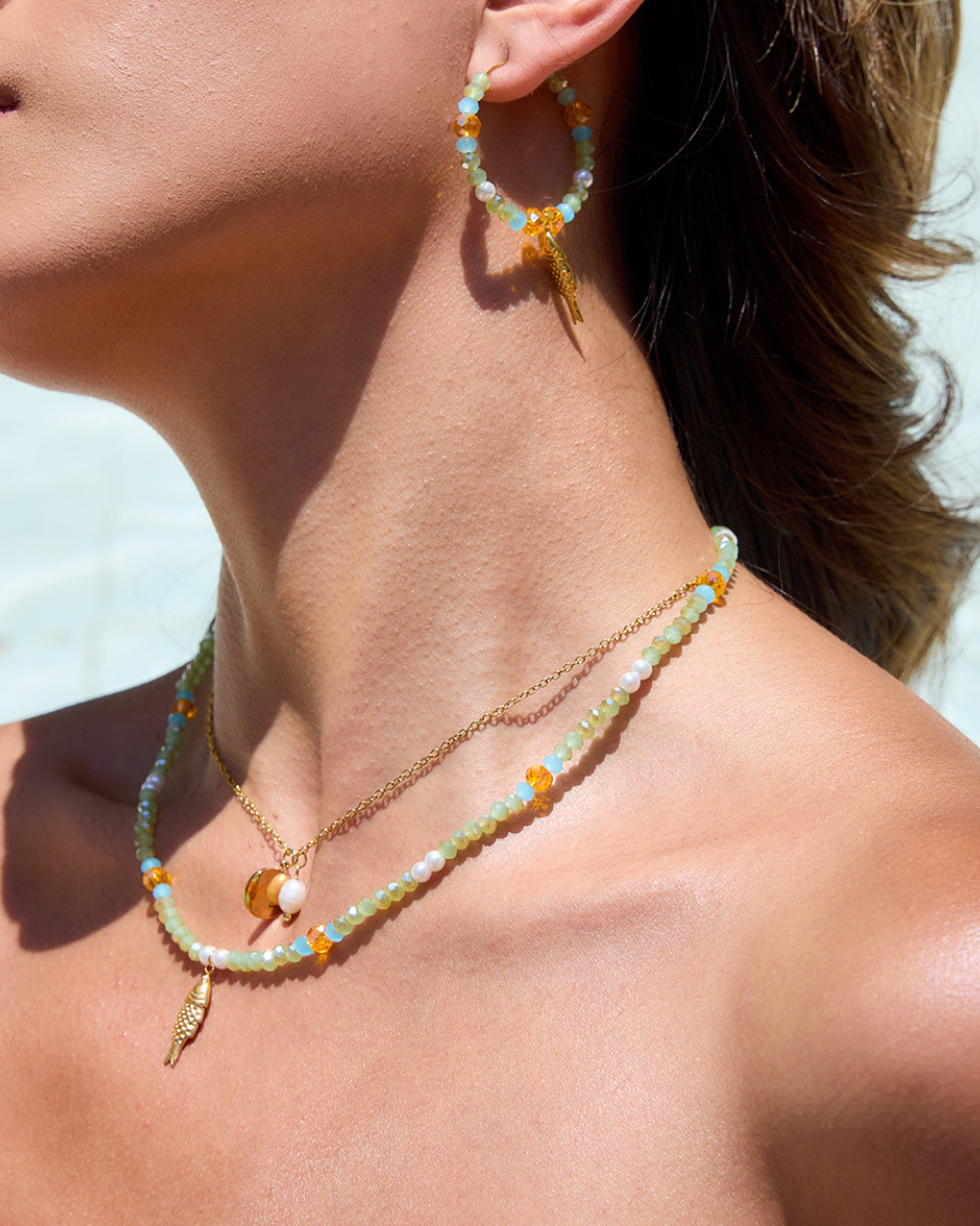 Close-up of a person wearing beaded earrings and necklaces against a light background