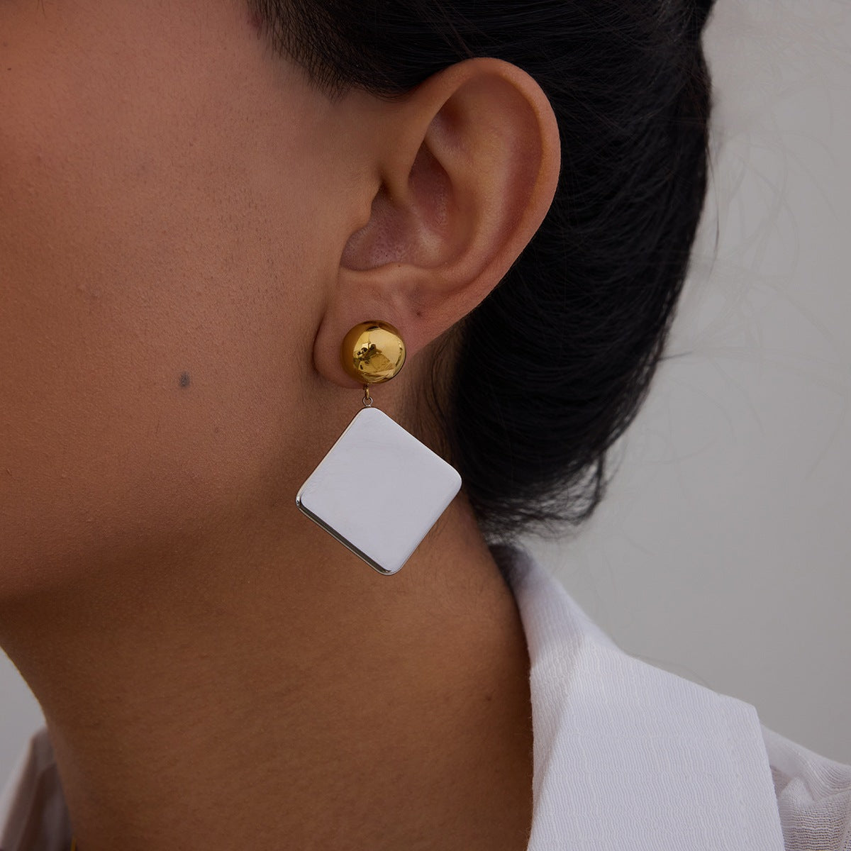 Model wearing gold and silver square earrings with polished finish