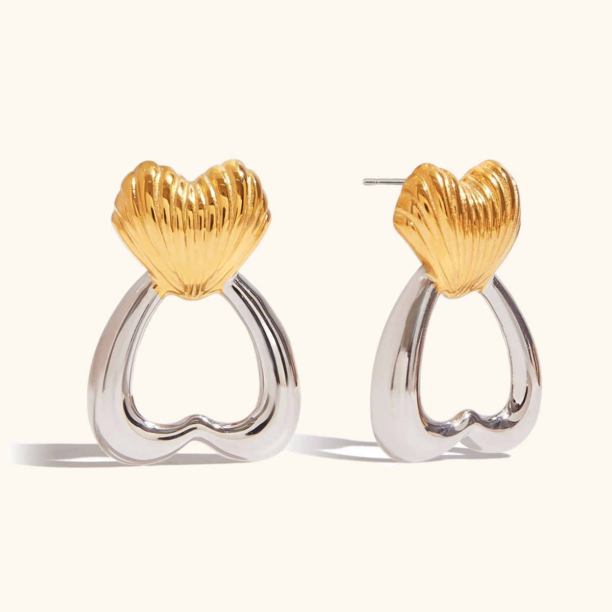 Close-up of gold and silver heart-shaped drop earrings with sculpted shell detail