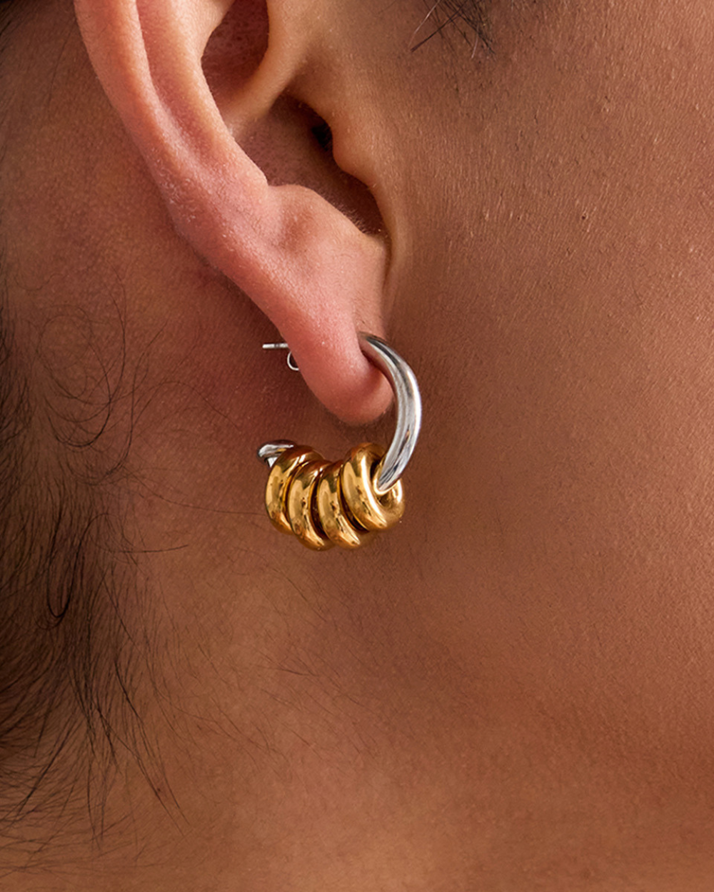 Close-up of an ear wearing a gold and silver hoop earring.