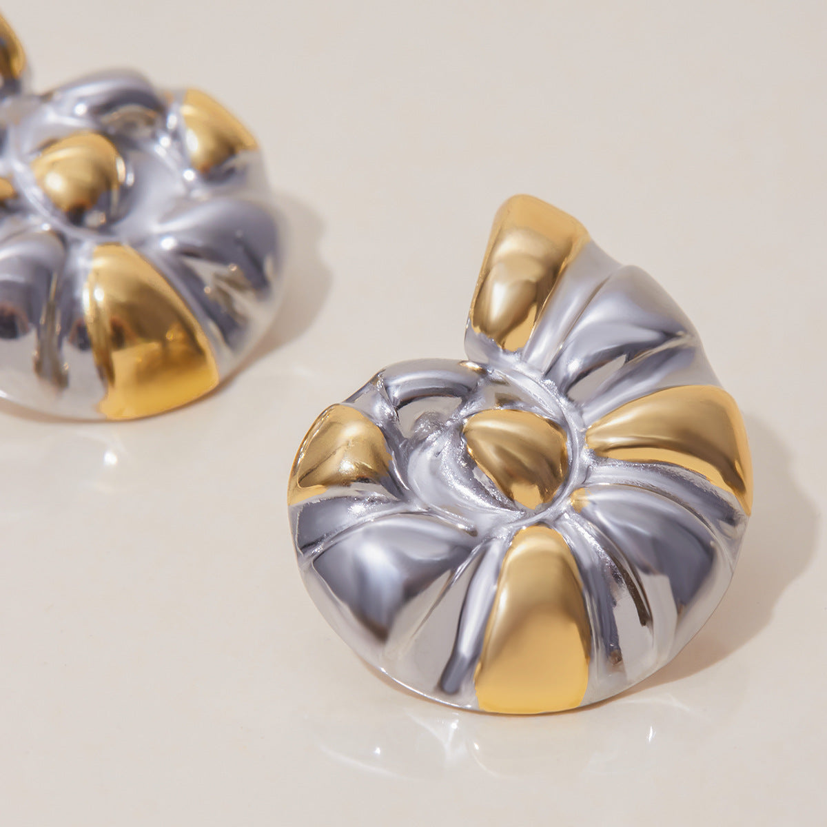 Close-up of nautilus shell design earrings with gold and silver glossy texture