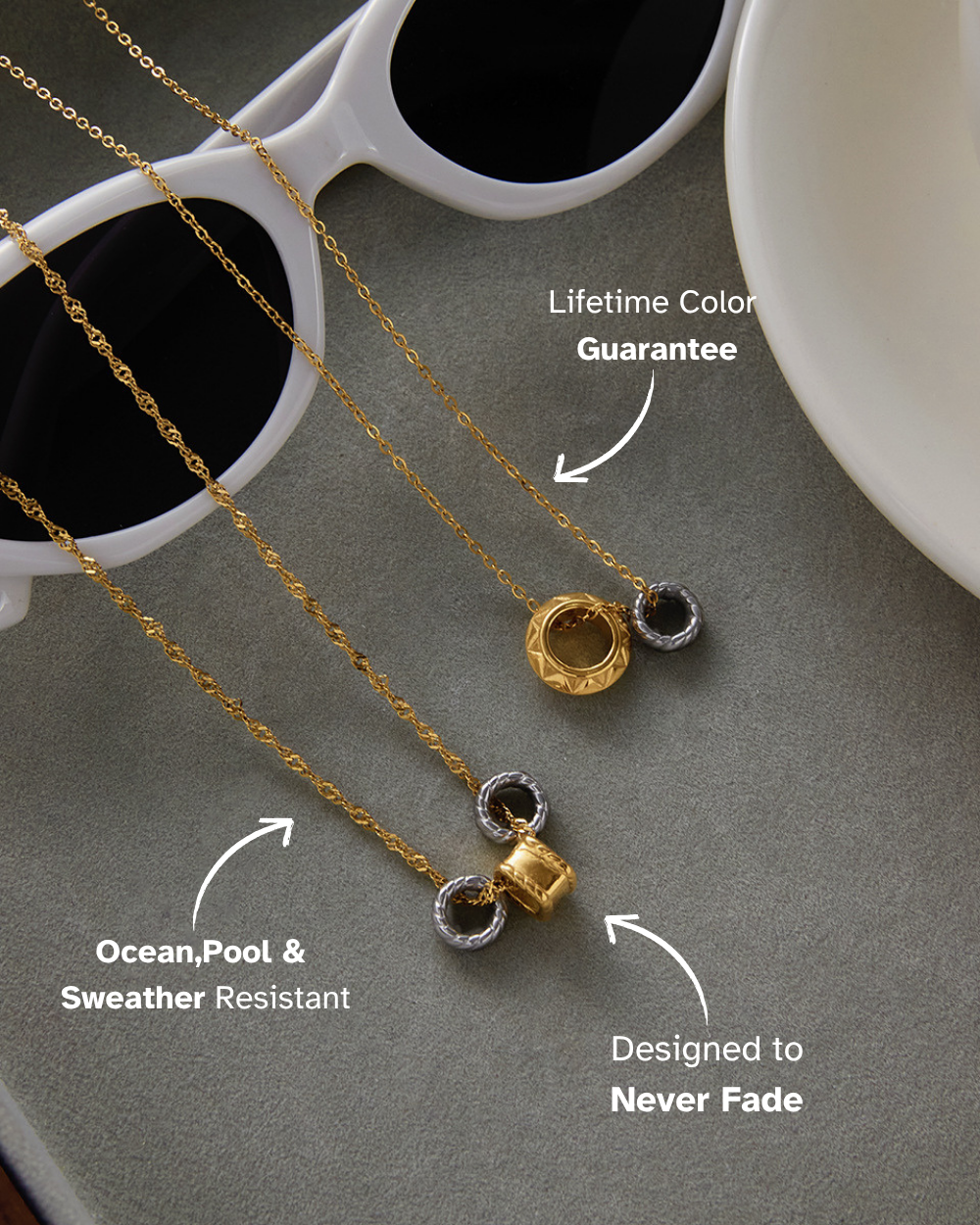 Gold necklace with black stones on a gray surface with sunglasses and a white cup in the background.