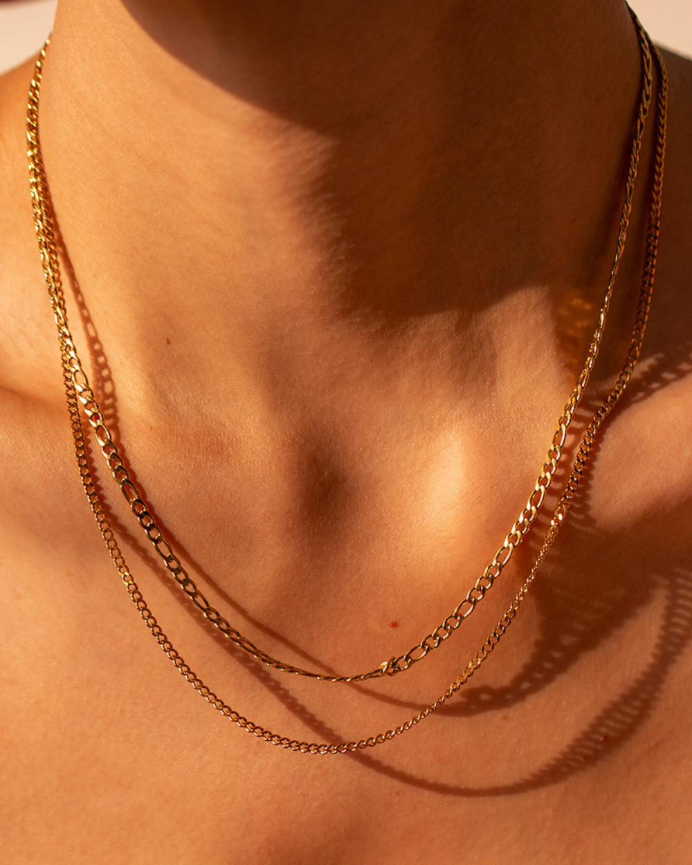 Gold chain necklace on a person's neck with a warm, sunlit background