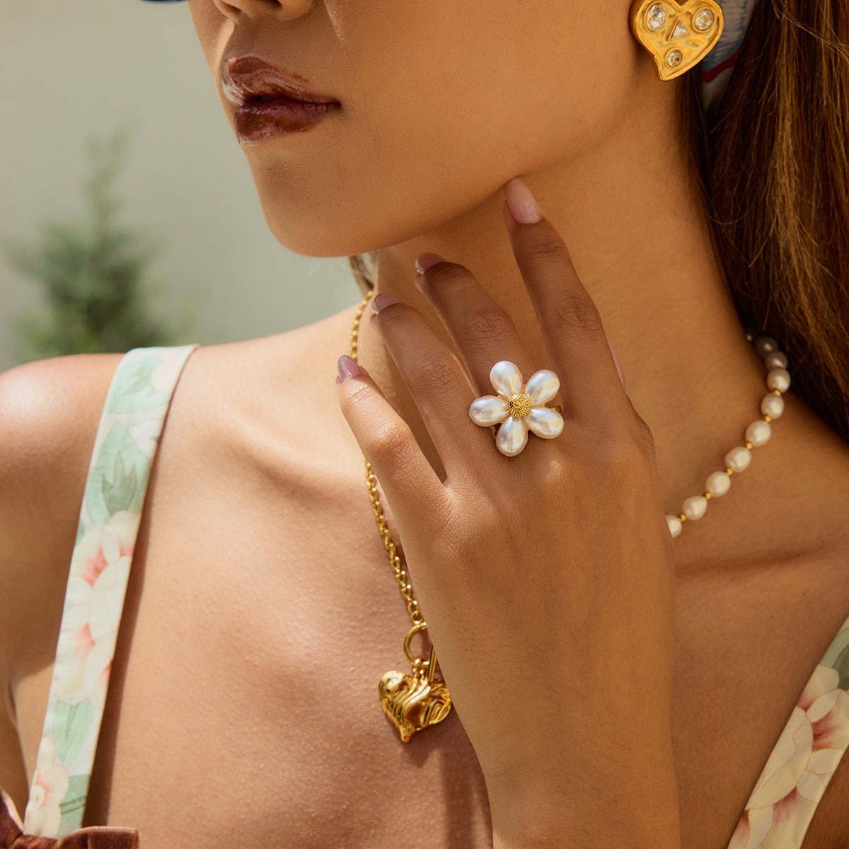 Model wearing statement pearl ring and layered gold jewelry in sunlight