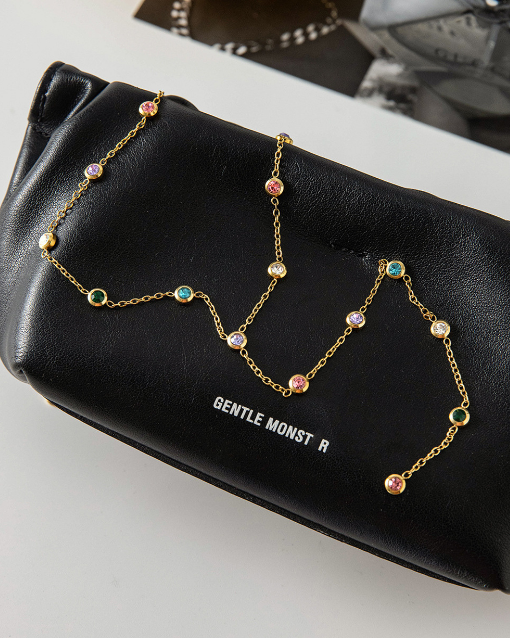 Gold chain necklace with colorful beads on a black pouch labeled 'GENTLE MONSTER'.