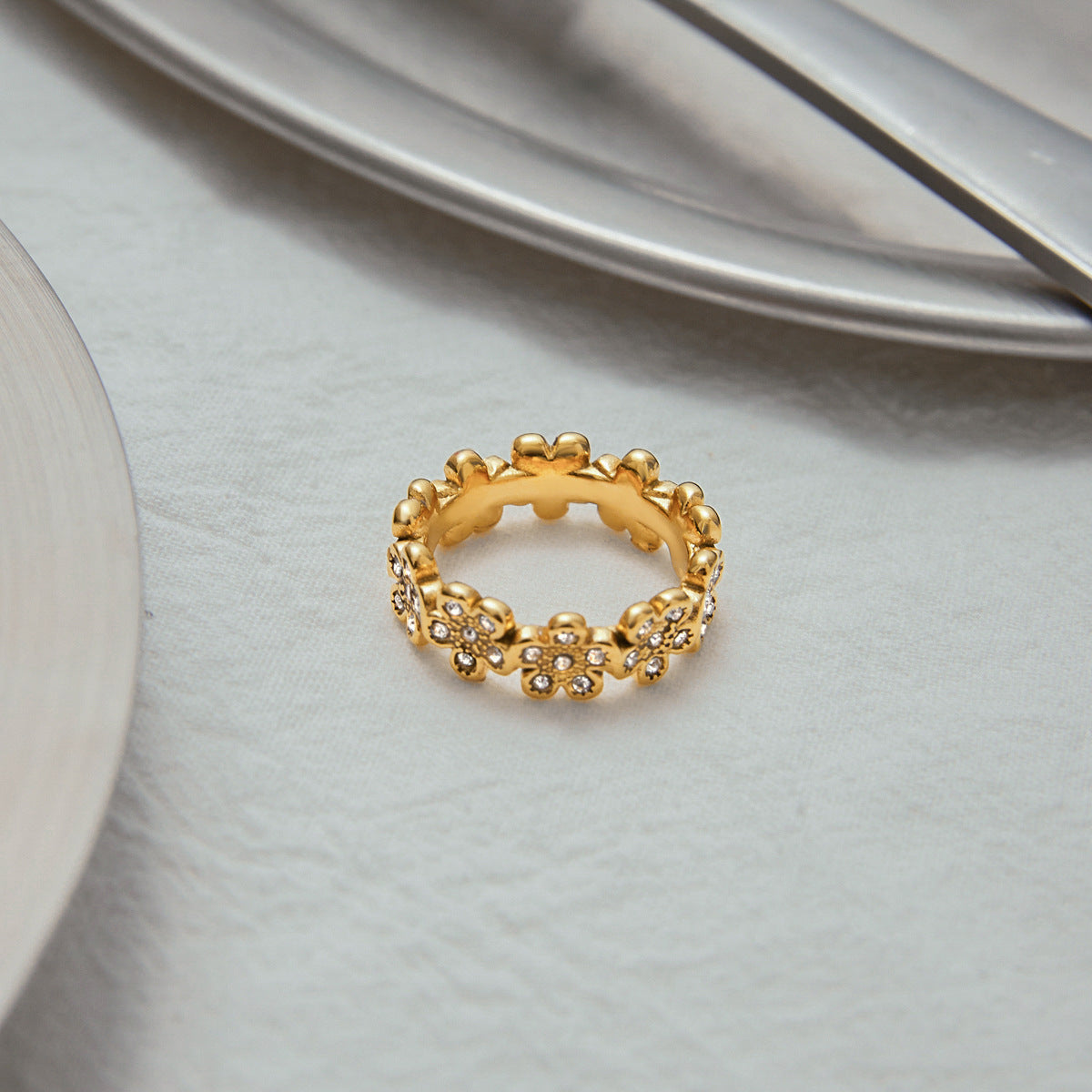 Gold flower ring on a textured table beside silver cutlery