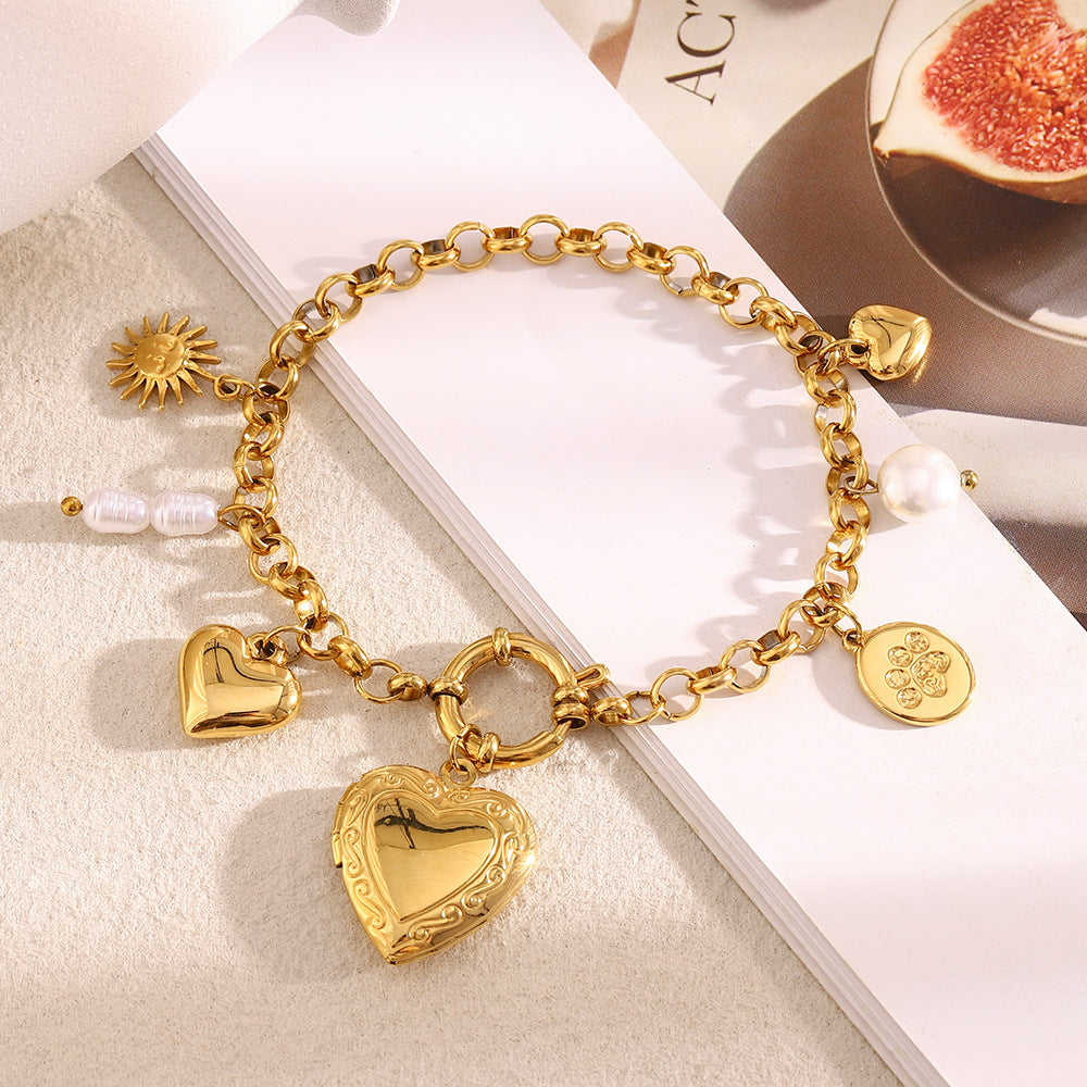 Gold chain bracelet with engraved heart locket and pearl charm on magazine background