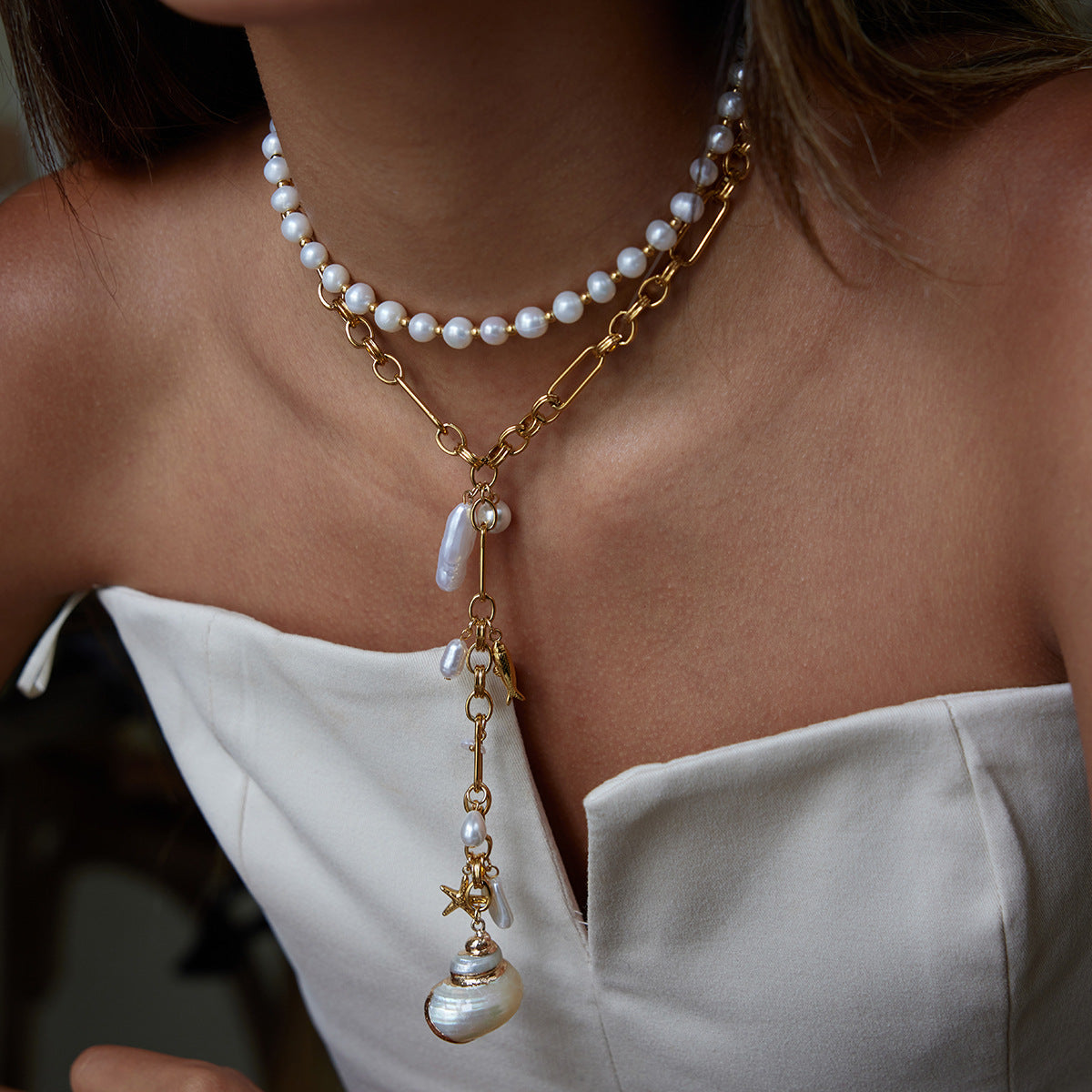Pearl necklace with gold chain and pendant on a person wearing a white top.