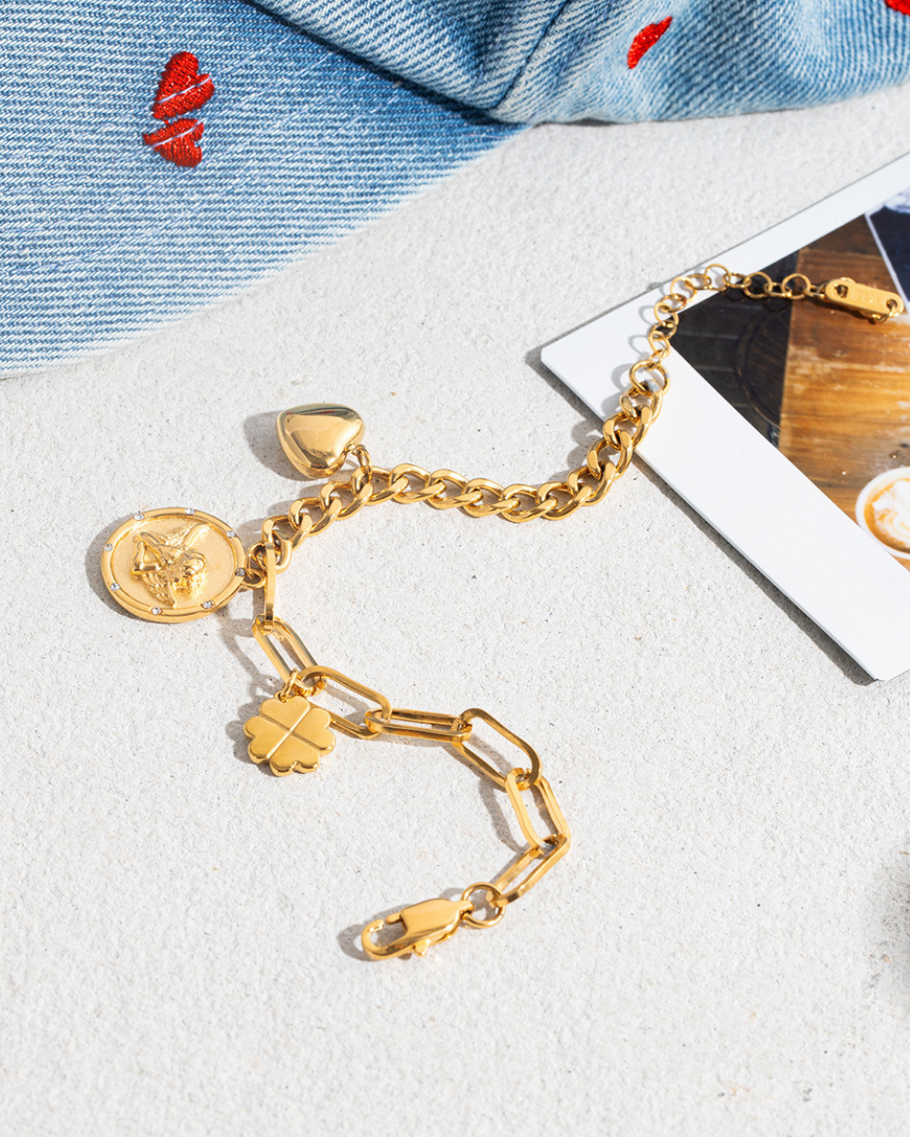 Gold bracelet with various charms on a white surface with denim fabric in the background