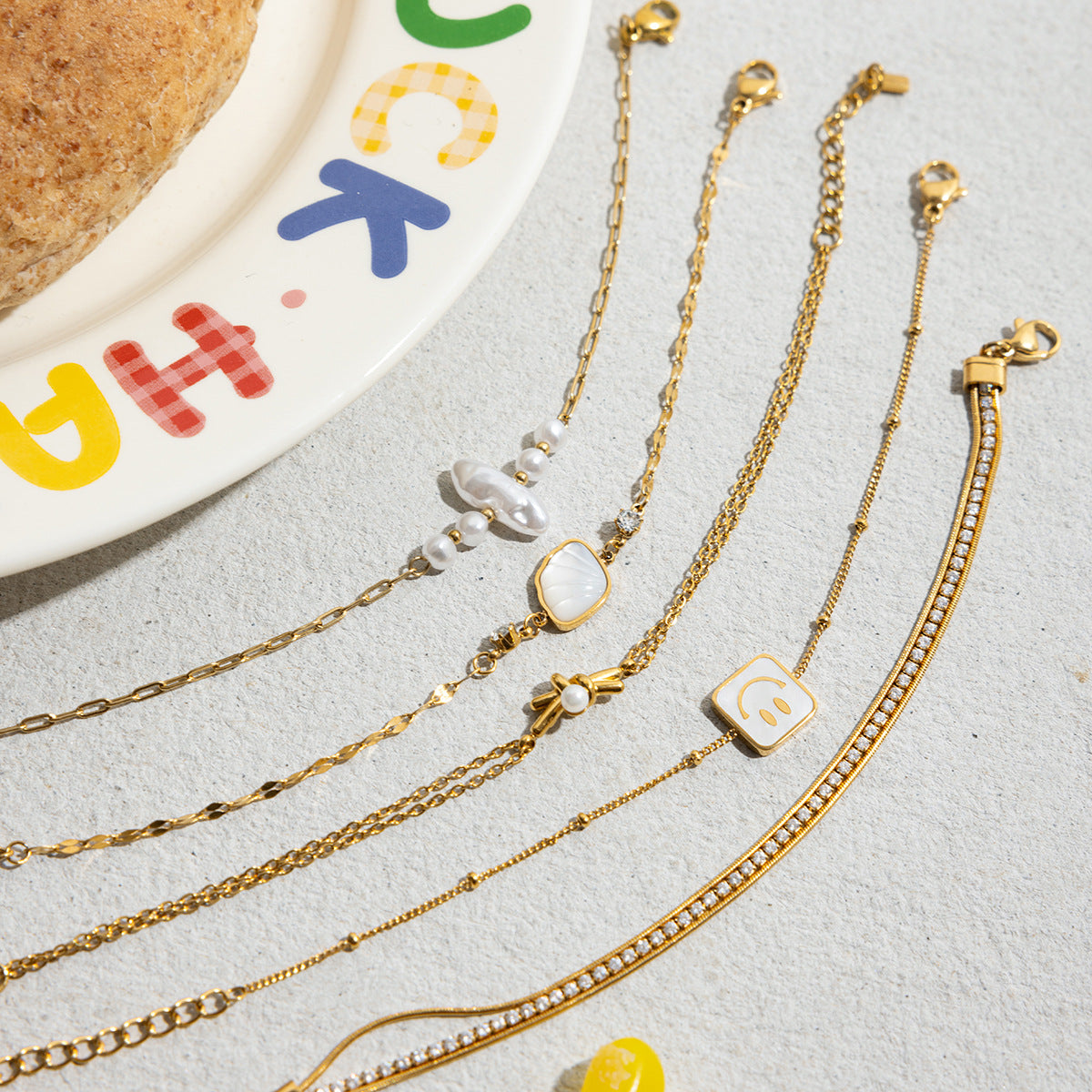 Gold bracelets with various charms on a light gray surface.