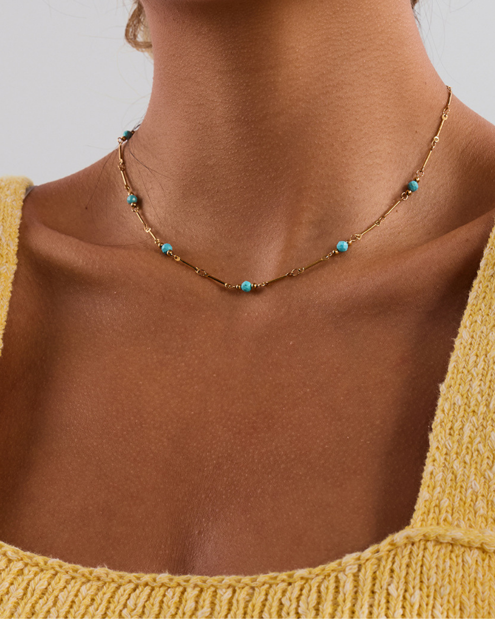 Necklace with turquoise beads worn by a person in a yellow top against a neutral background
