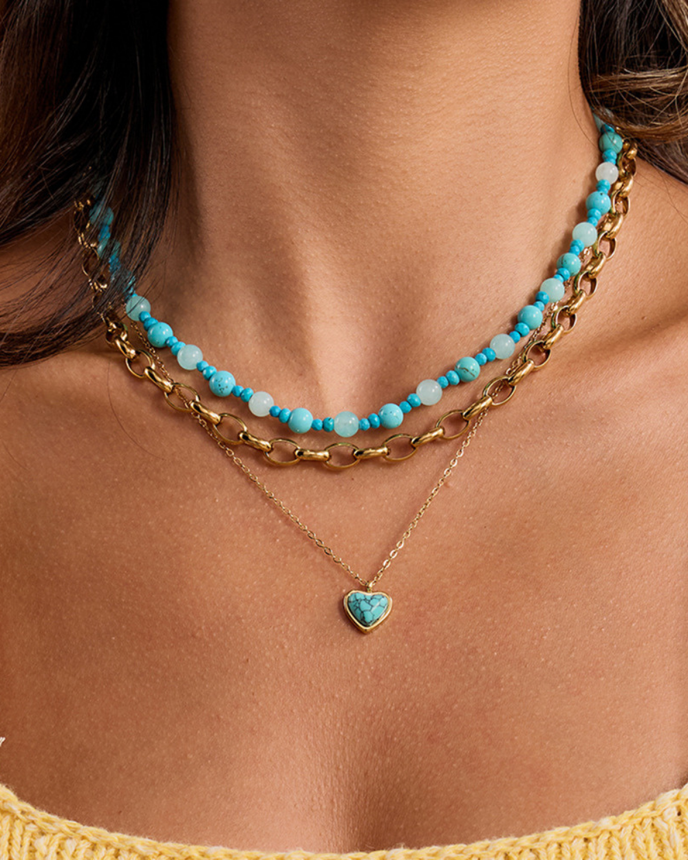 Necklace with turquoise beads and gold chain on a person wearing a yellow top.