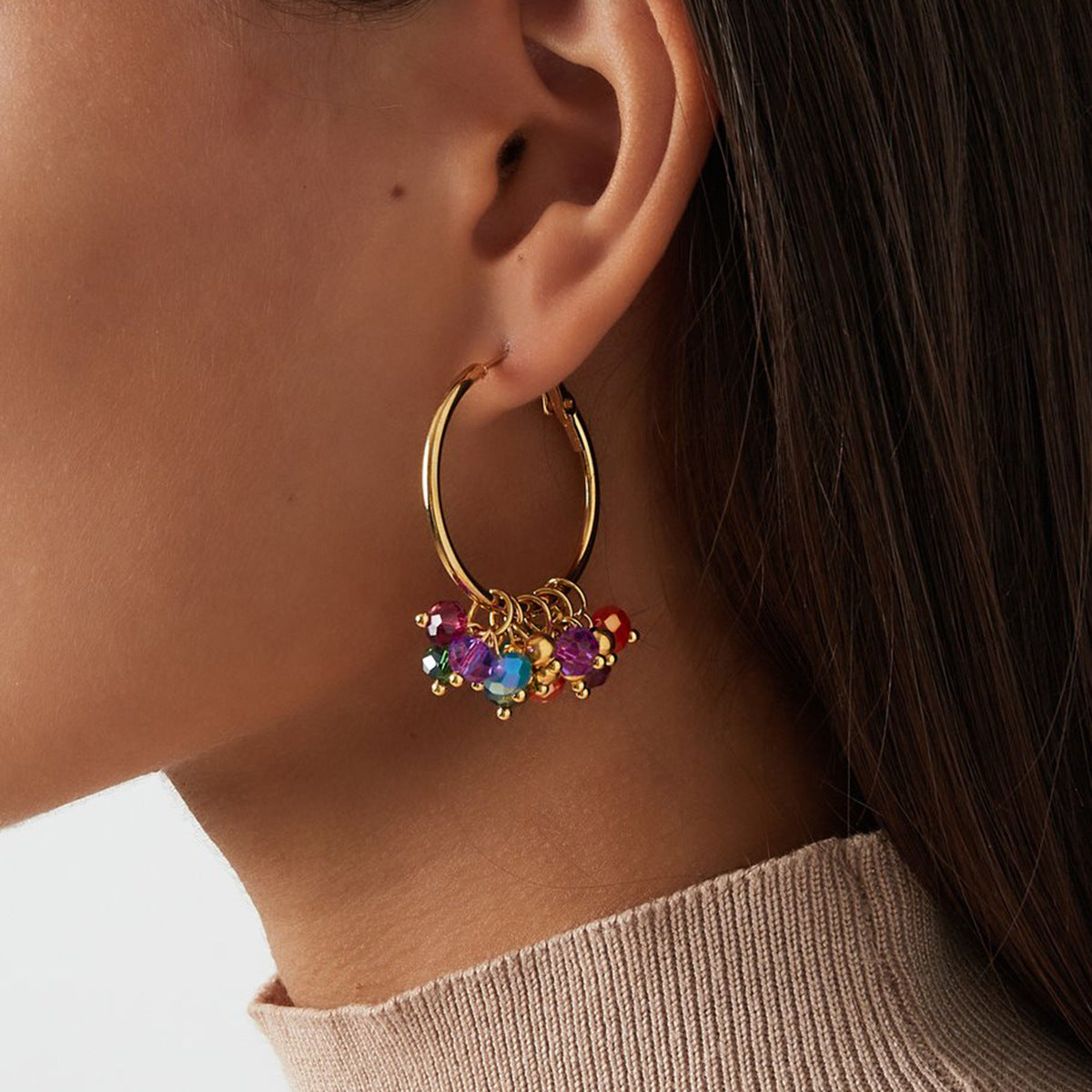 Gold hoop earring with colorful beads worn by a person