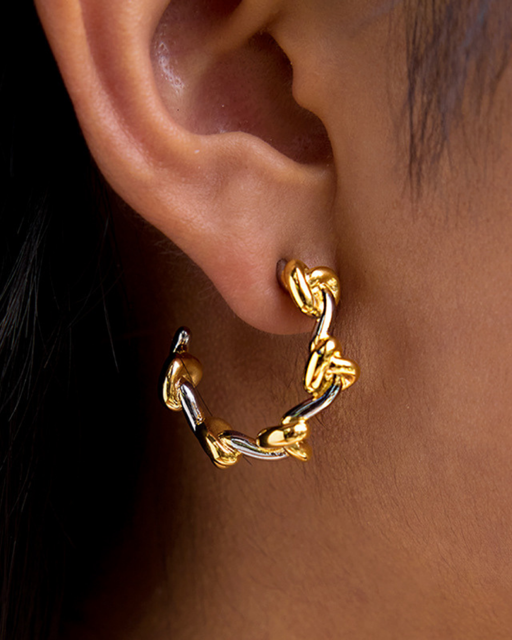 Gold hoop earring worn on an ear with a close-up view