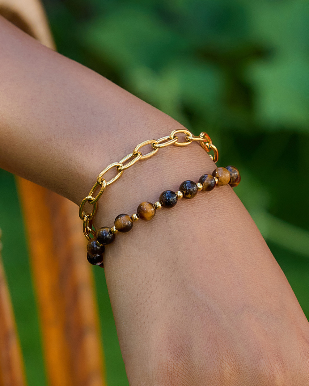 Gold chain bracelet with tiger eye beads on a wrist against a blurred green background