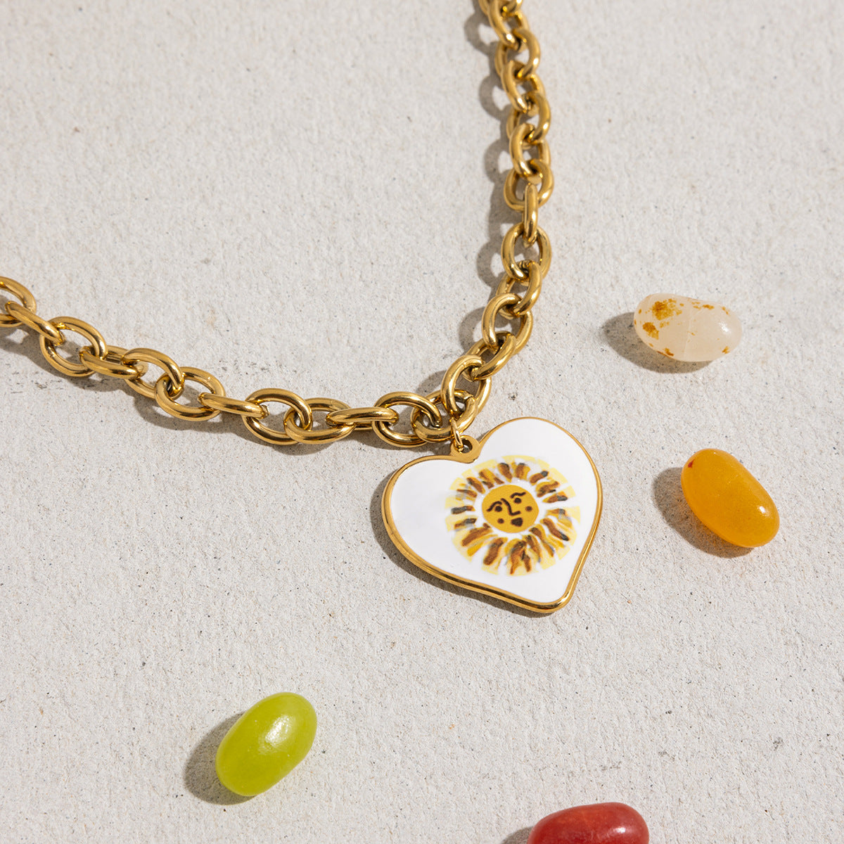Bold gold link chain necklace with white enamel sun pendant styled with candies