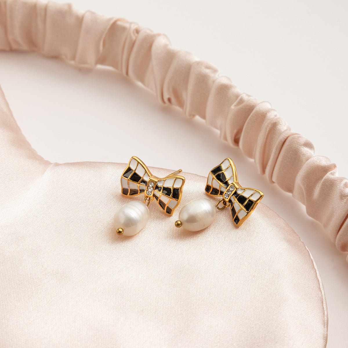 Bow-shaped earrings with pearl centers on a beige headband.