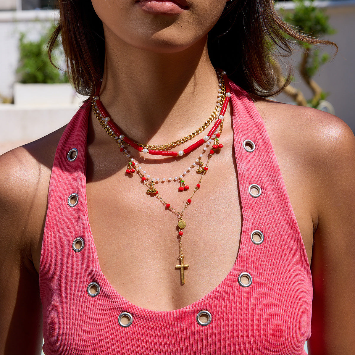 Close-up of a person wearing a pink top with grommet details and multiple necklaces.