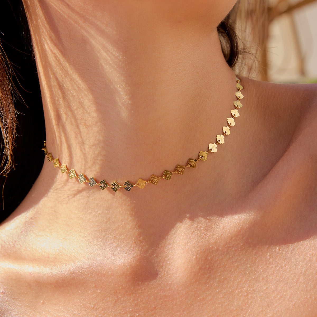 Model wearing gold shell choker necklace under beach sunlight close-up