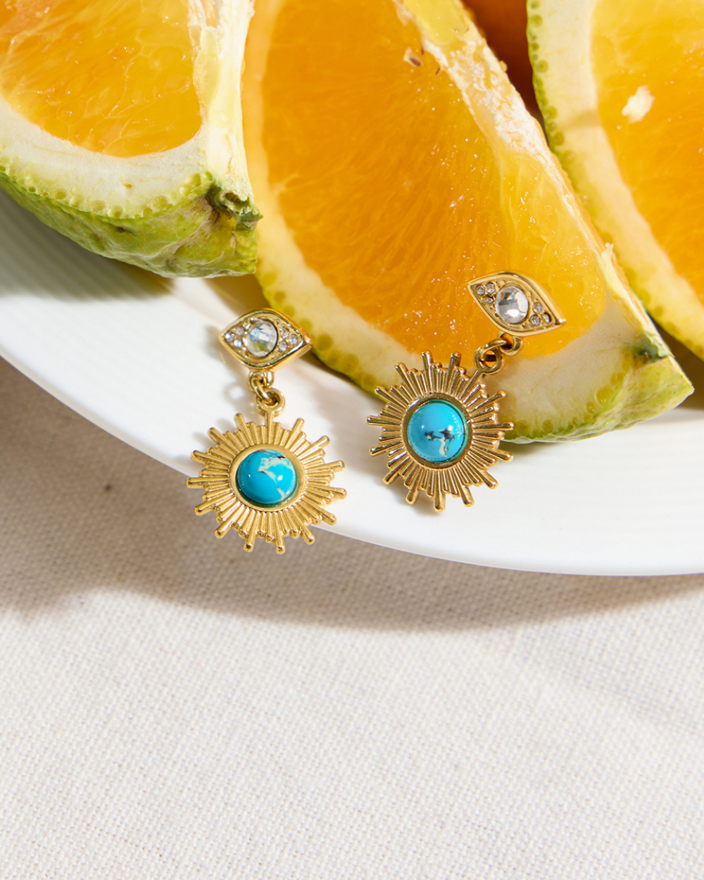 Gold earrings with turquoise stones on a plate with sliced oranges