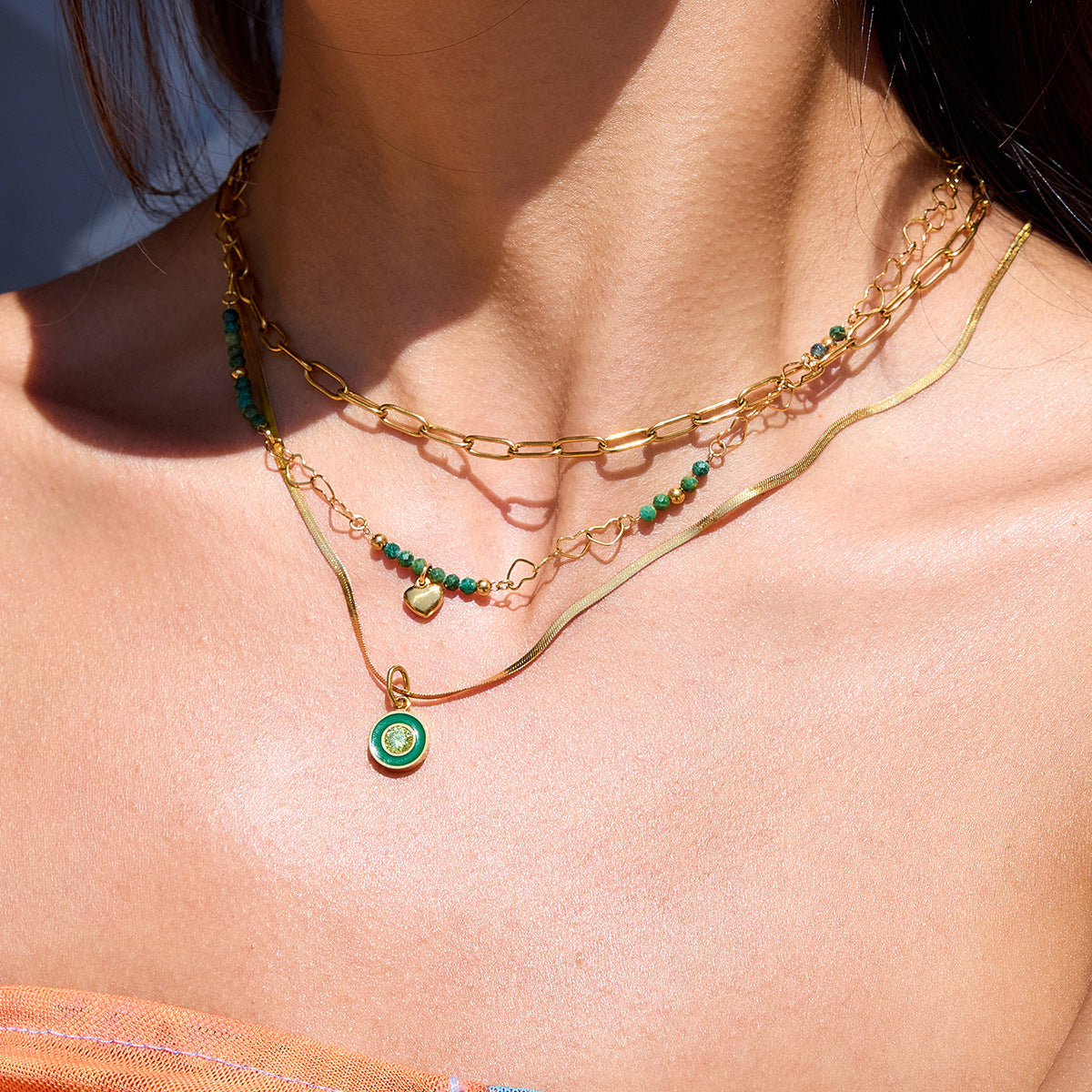 Model wearing layered gold and green necklaces with beachwear