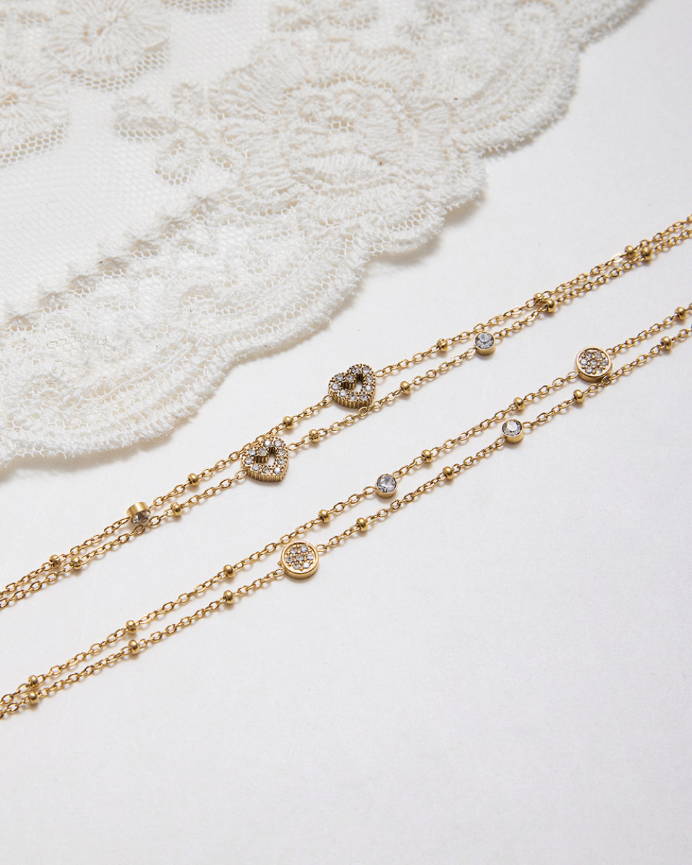 Two gold necklaces with diamond accents on a white lace background