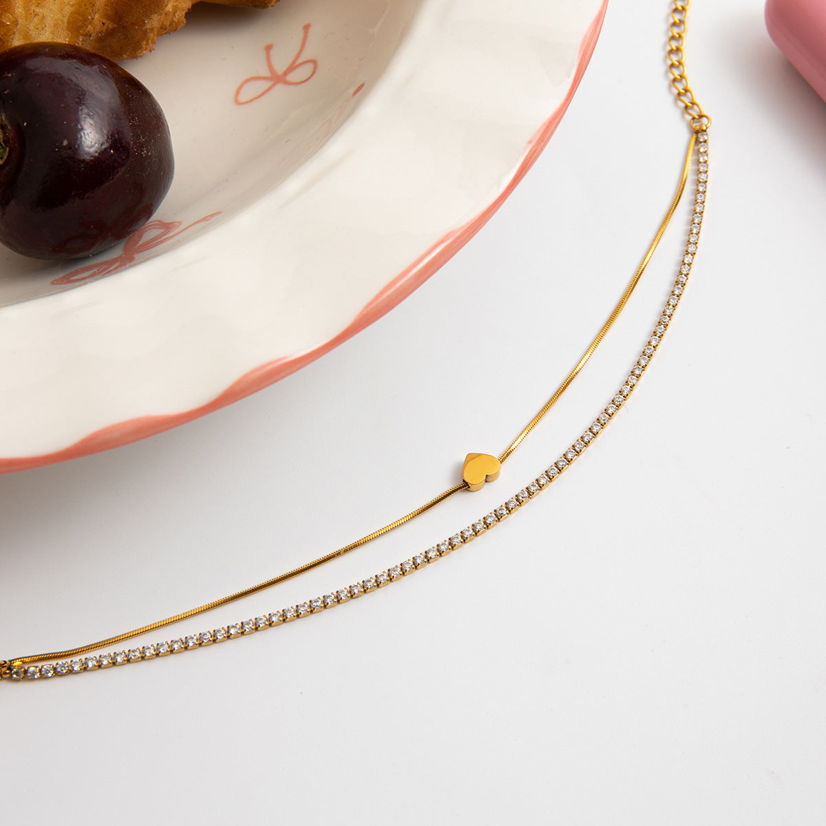 Gold necklace with a heart pendant on a white surface with a cherry and plate in the background.