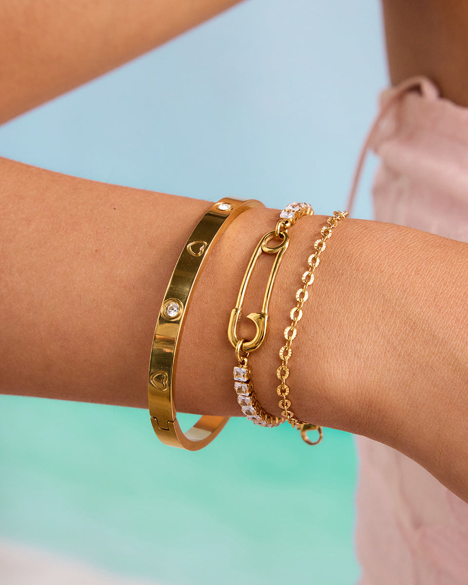 Woman wearing three gold bracelets, including a rhinestone safety pin chain, styled for summer