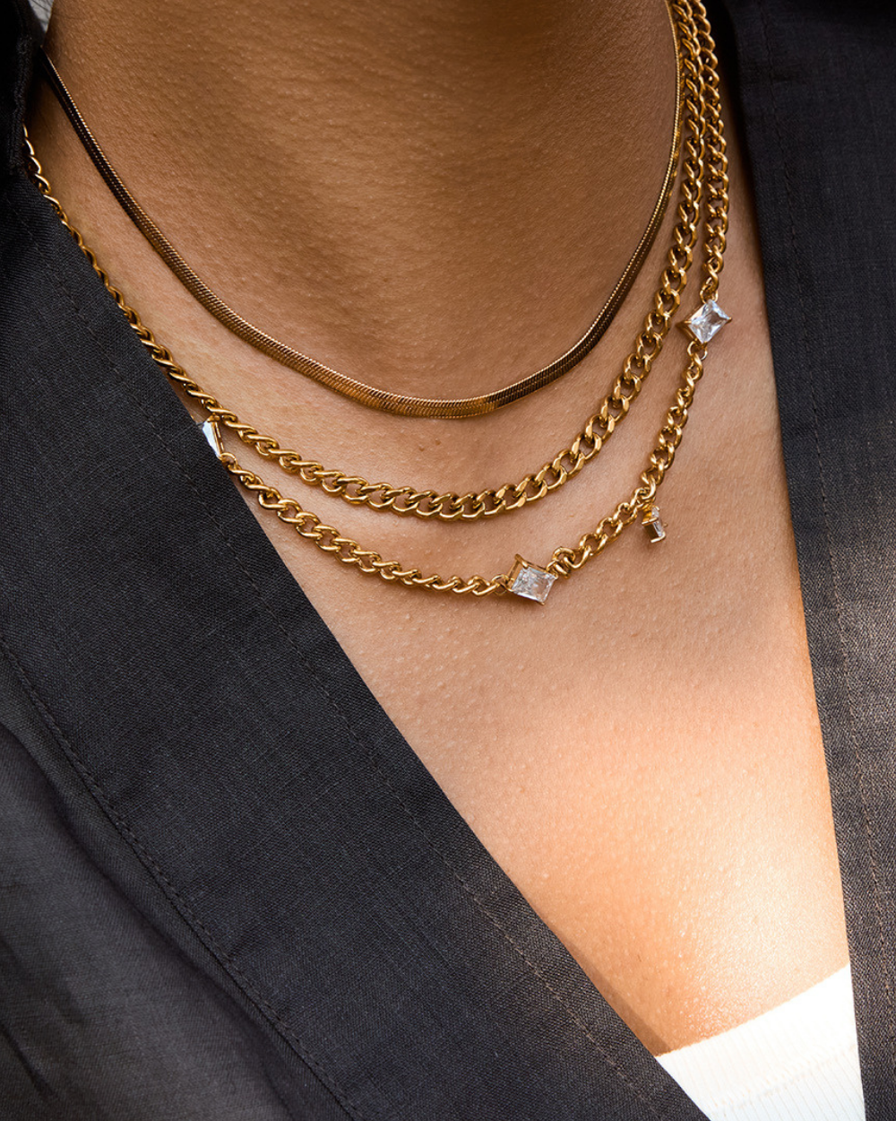 Gold chain necklaces with diamond pendants on a person wearing a black blazer.