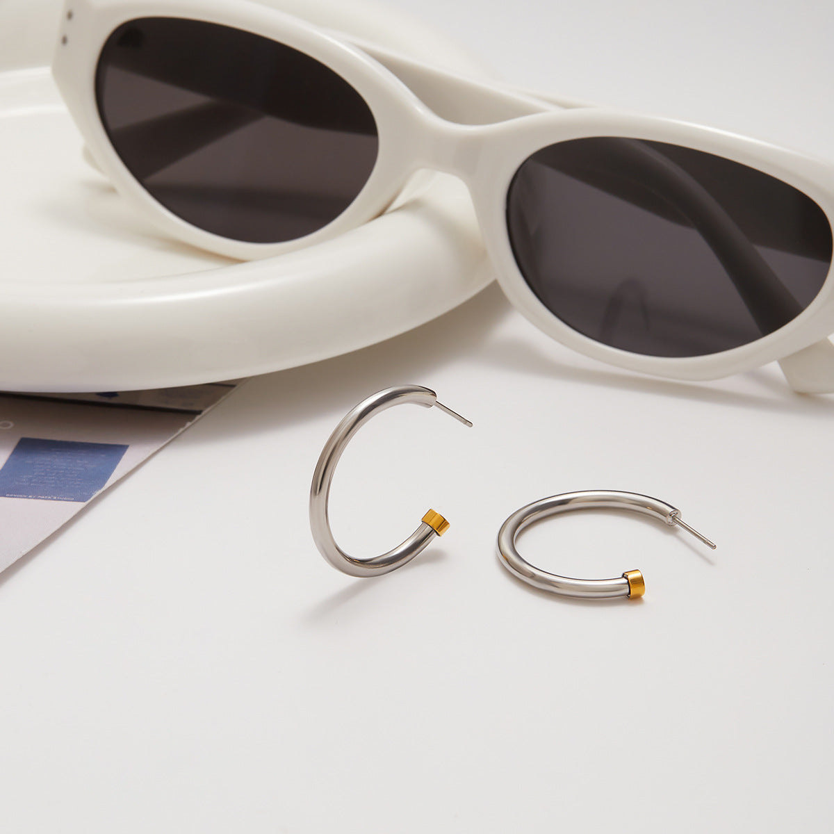 Silver hoop earrings with gold accents on a white surface with sunglasses in the background.