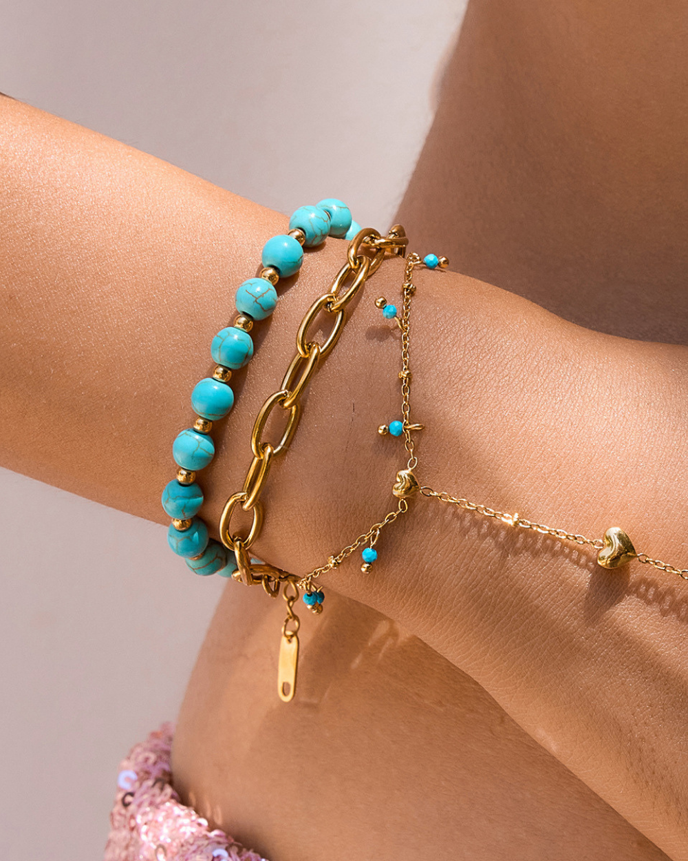 Turquoise beaded bracelet and gold chain bracelet on a wrist against a neutral background