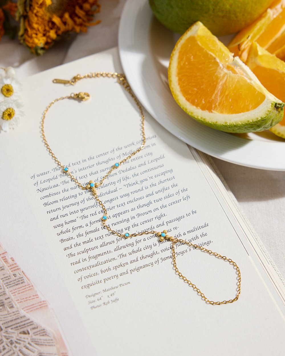 Gold necklace on an open book with oranges and flowers in the background