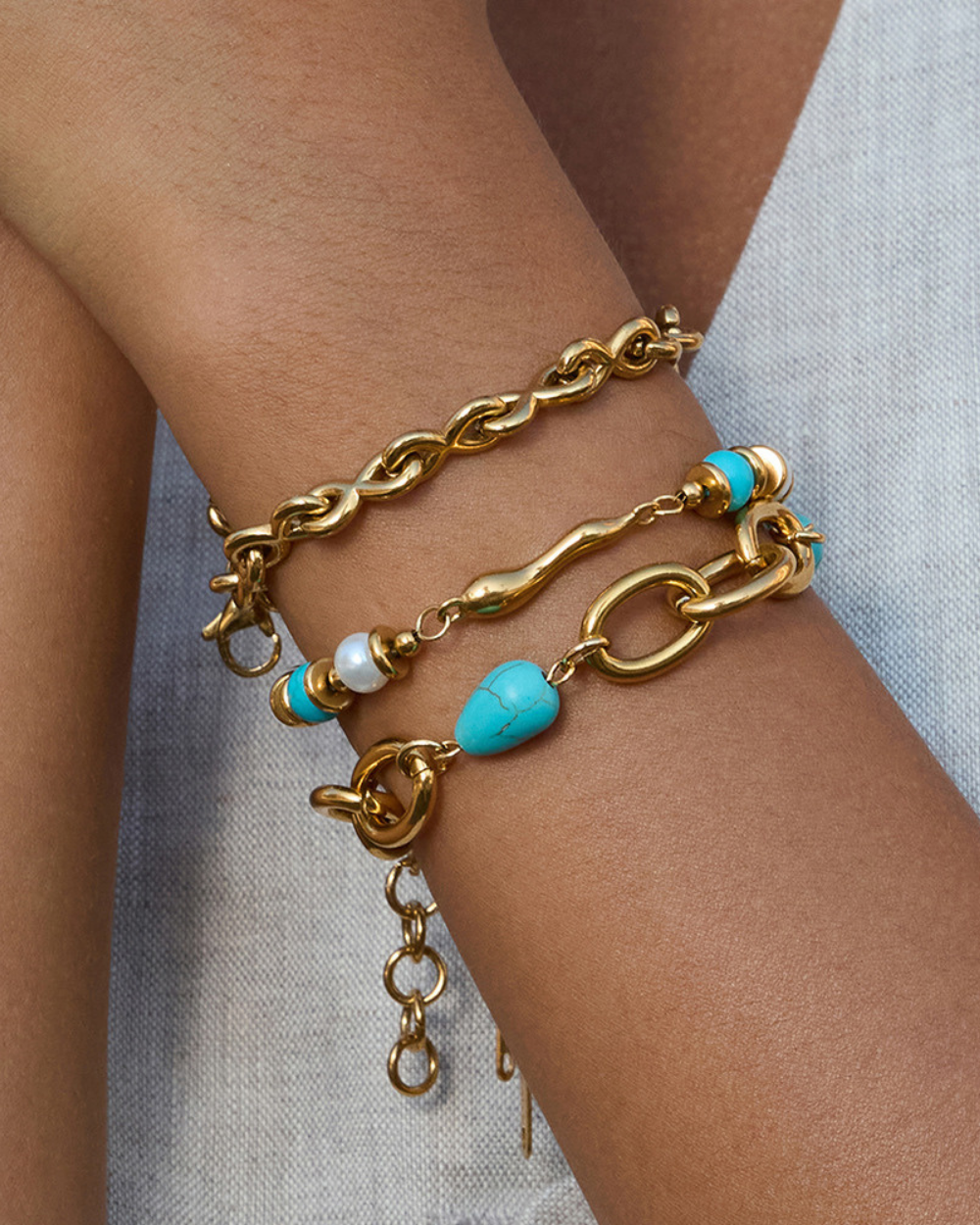 Gold chain bracelet with turquoise beads on a wrist against a neutral background