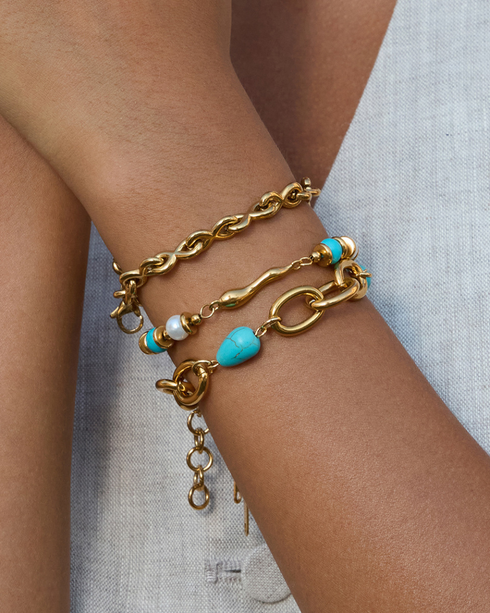 Gold bracelet with turquoise beads on a wrist against a light background