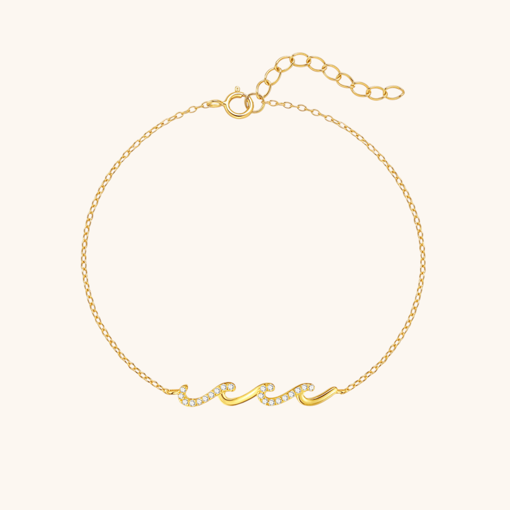 Thin gold bracelet with wave-shaped crystal detail, laid flat on white background