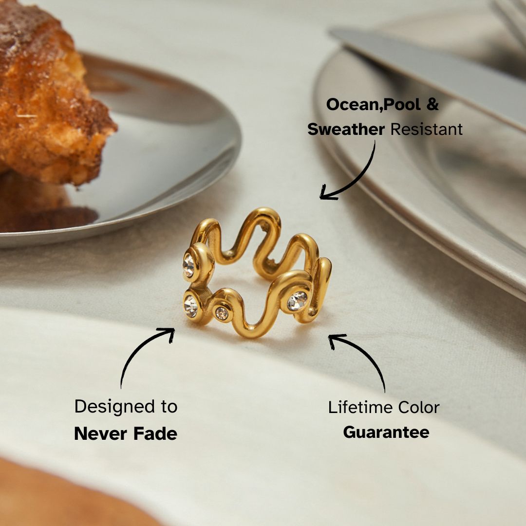 Gold wavy crystal ring on a ceramic plate next to croissant and silverware