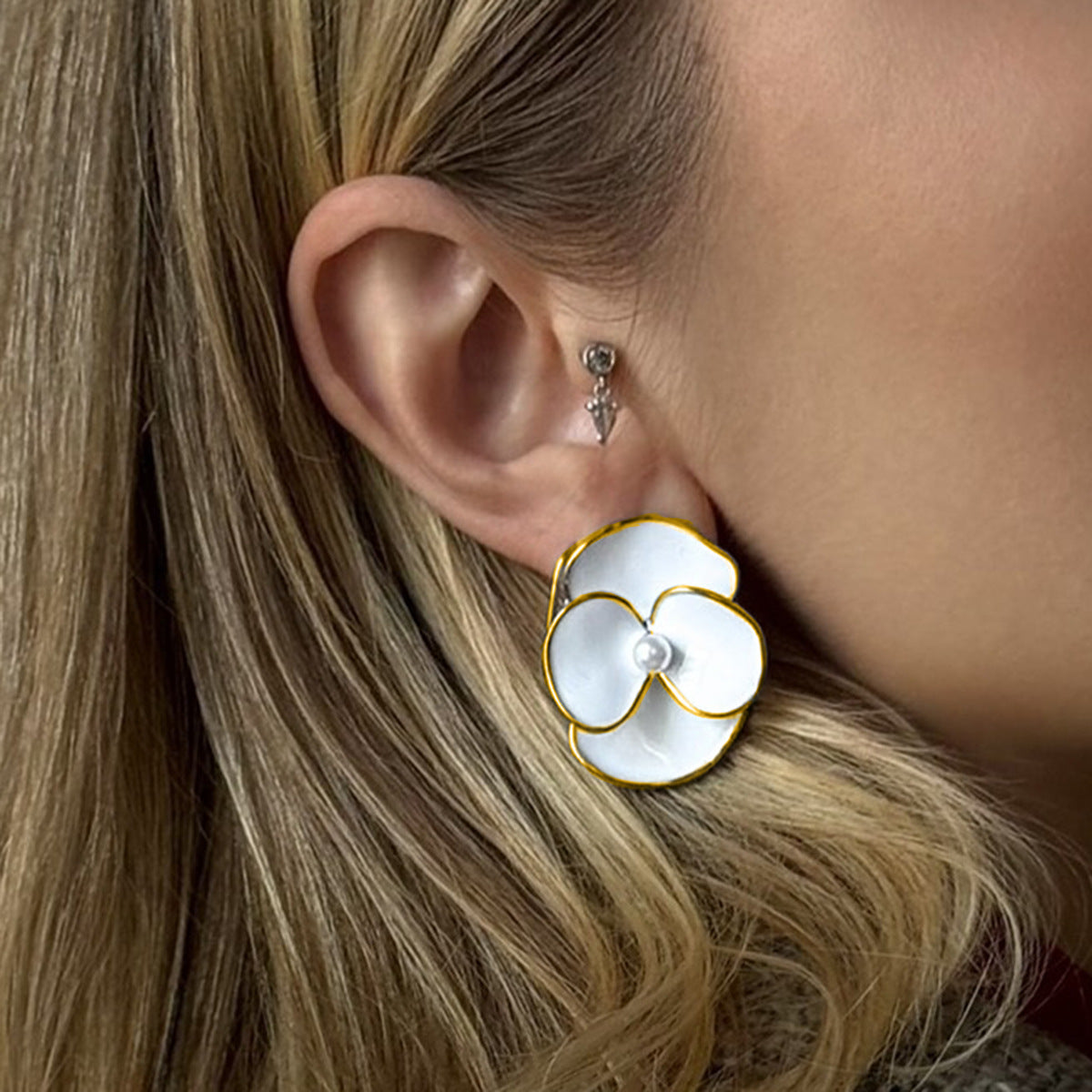 Close-up of white flower enamel earrings with pearl center on model's ear