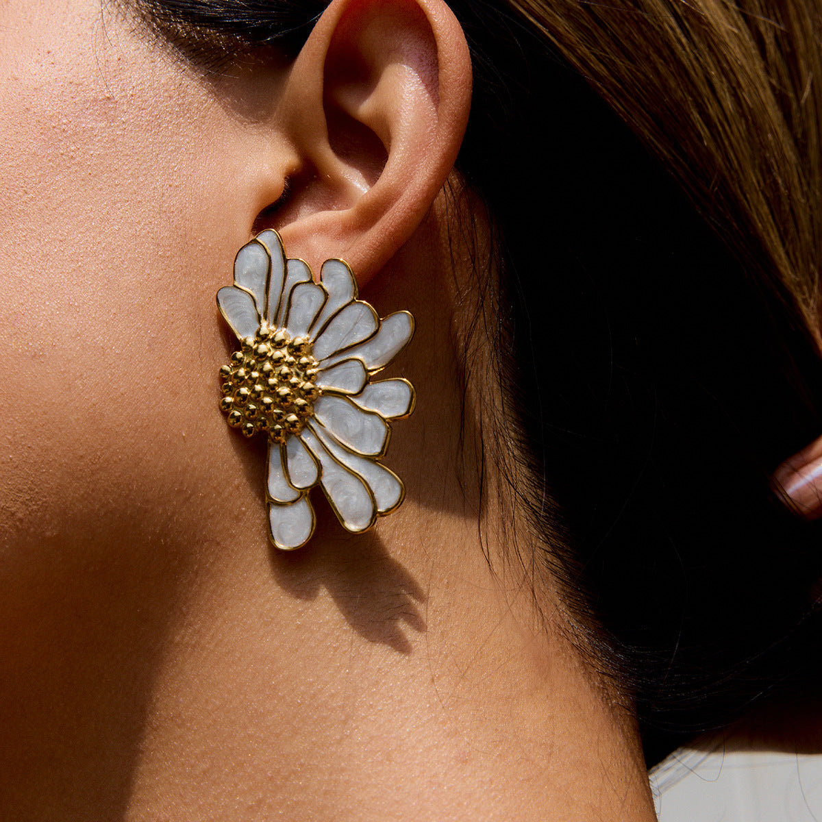 Close-up of white daisy earrings with gold center on model’s ear