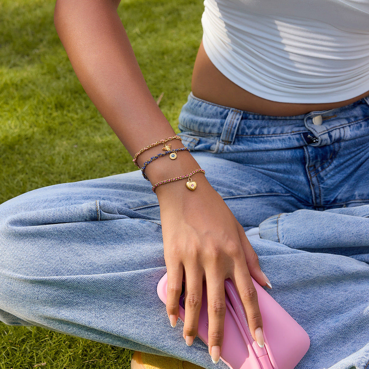 Person sitting on grass wearing a white shirt and blue jeans, holding a pink object.
