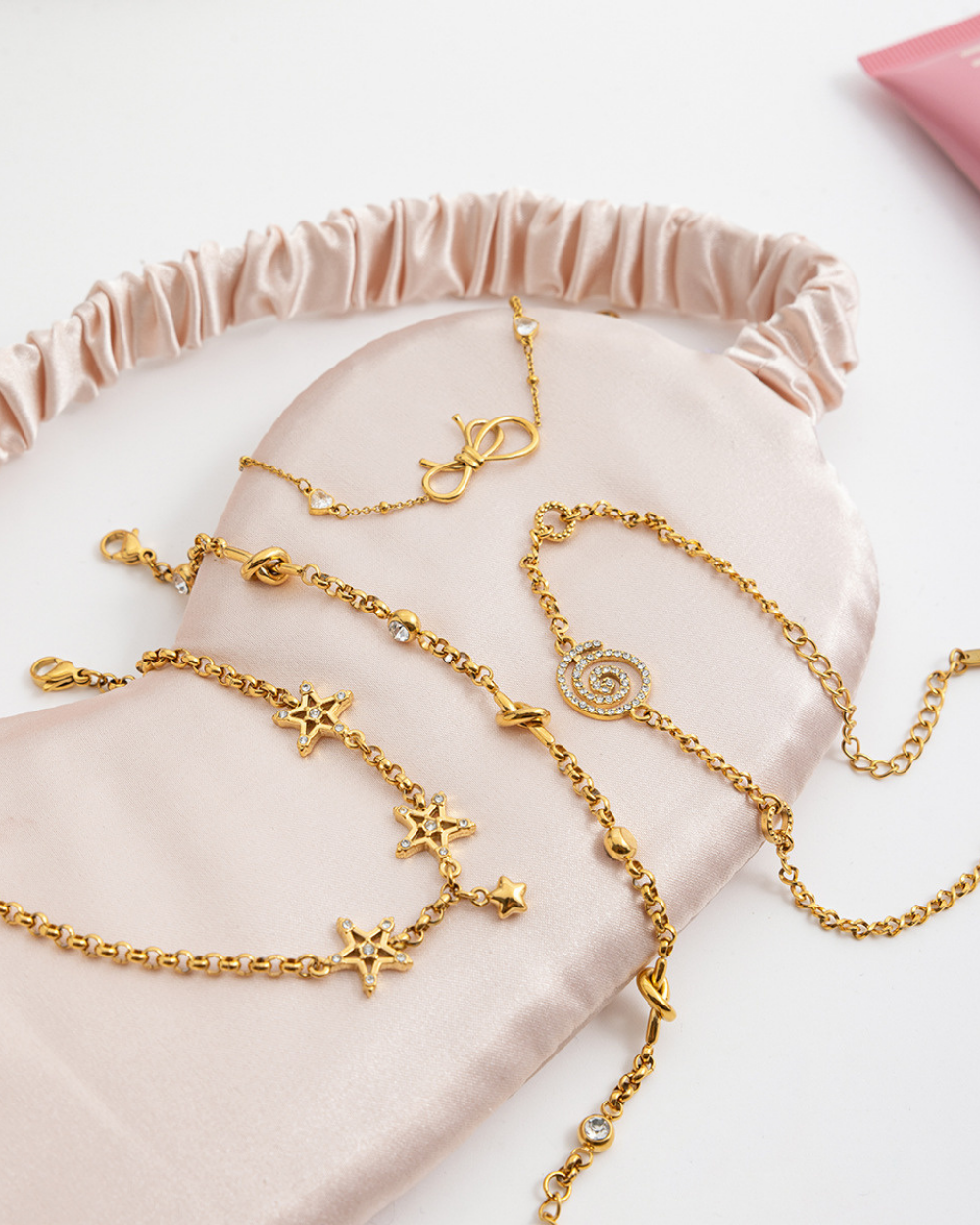 Gold bracelets with star and chain designs on a pink fabric background