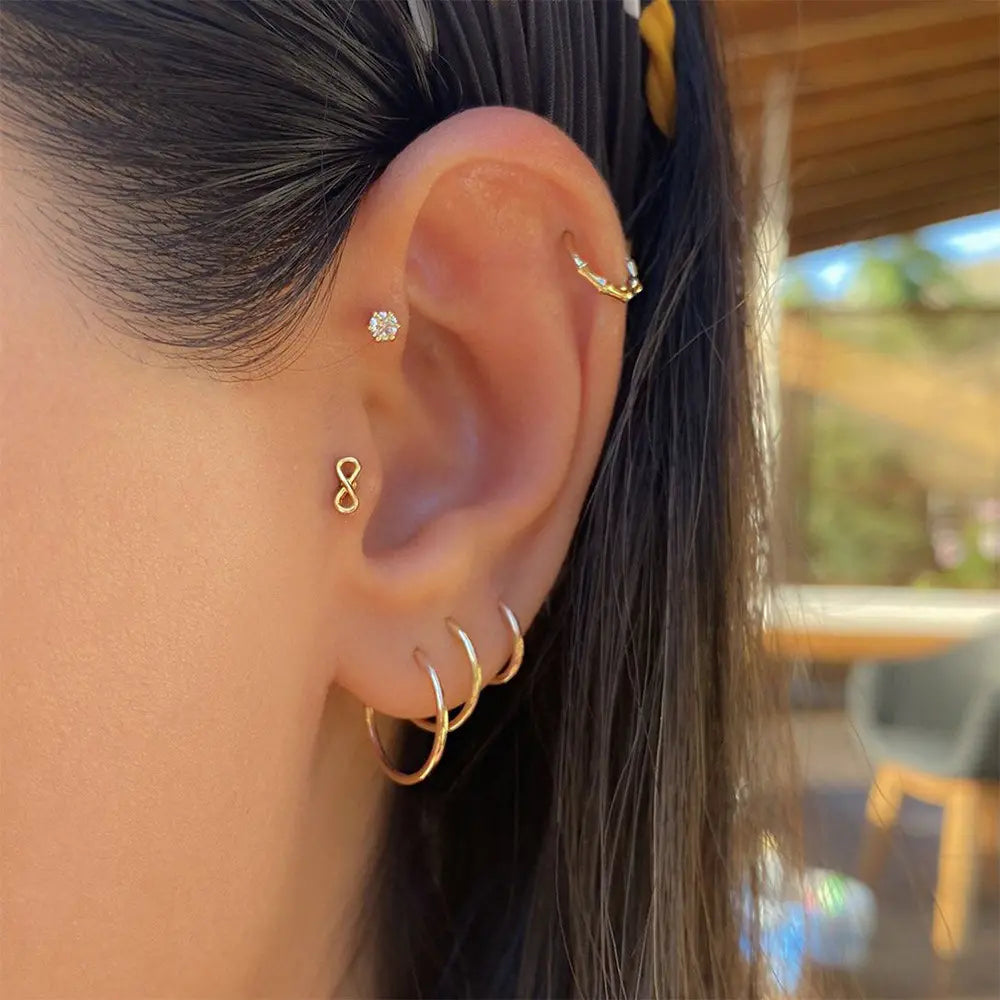 Model wearing delicate 14k gold-plated infinity stud earrings, with a close-up of the earring in the ear for a modern, minimalistic look.