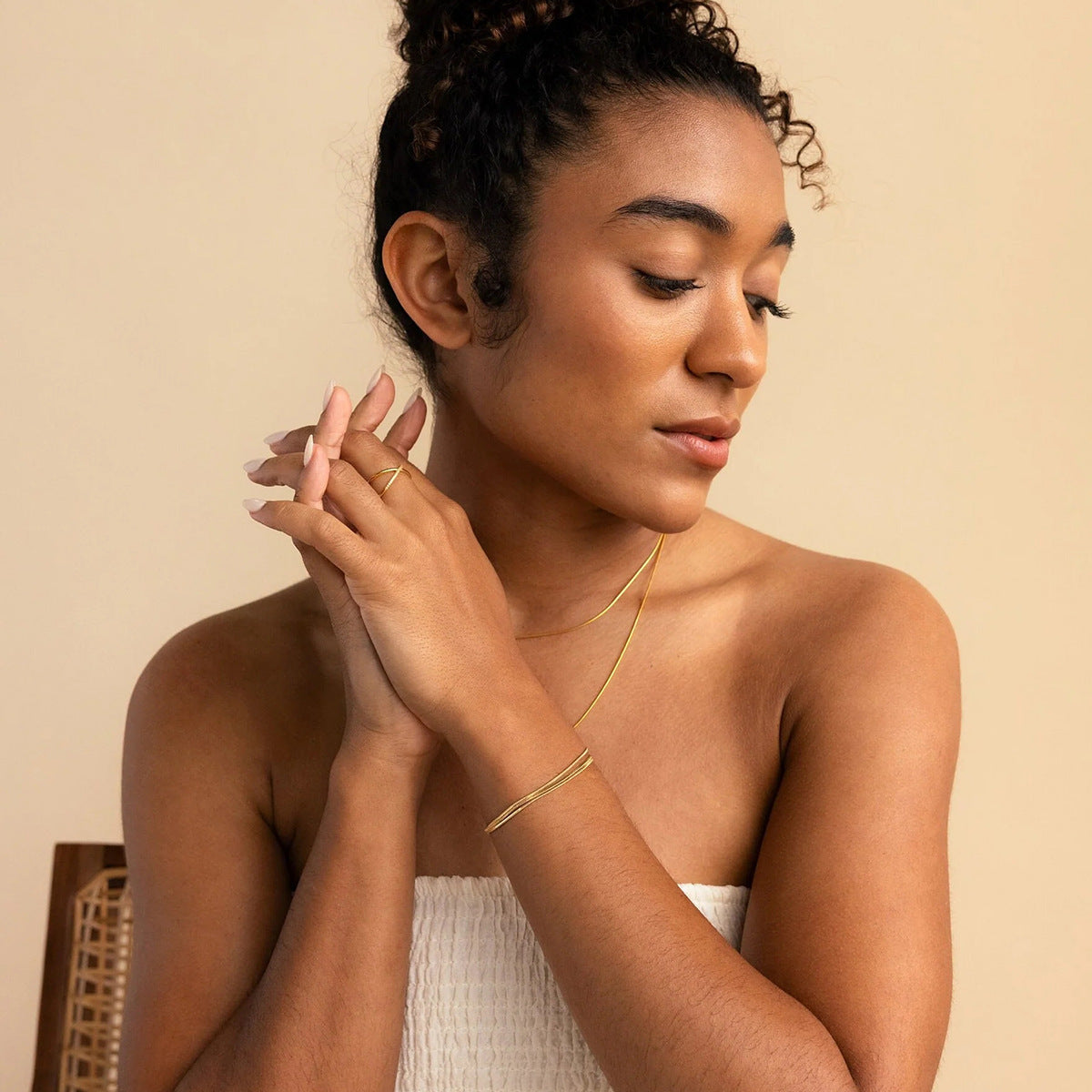 Female model wearing delicate gold bracelet with soft nude tones