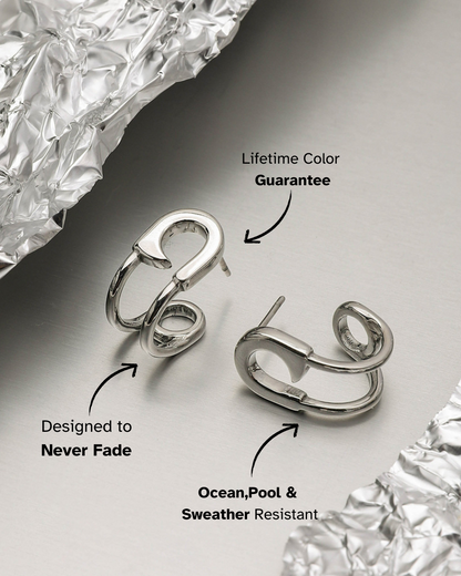 Silver hoop earrings on a reflective surface with text about color guarantee and weather resistance.