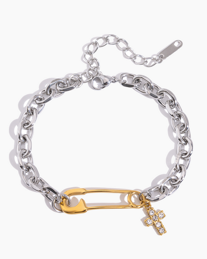 Silver chain bracelet with a gold safety pin and cross charm on a white background