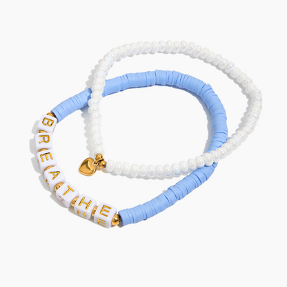 Two beaded bracelets, one white with gold letters and the other blue, on a white background.