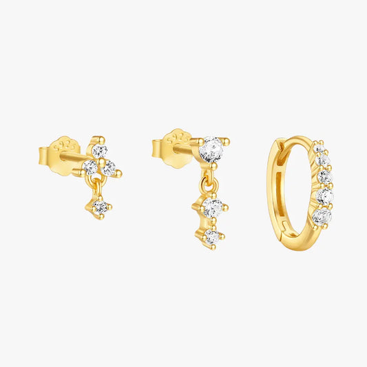 A set of three gold earrings featuring clear gemstones: a small stud, a dangling gem with three connected stones, and a gold hoop earring adorned with sparkling gems.