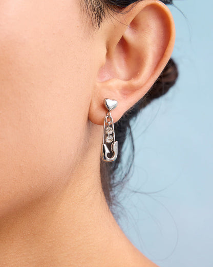 Silver earring with a heart and fish design worn by a person against a light blue background