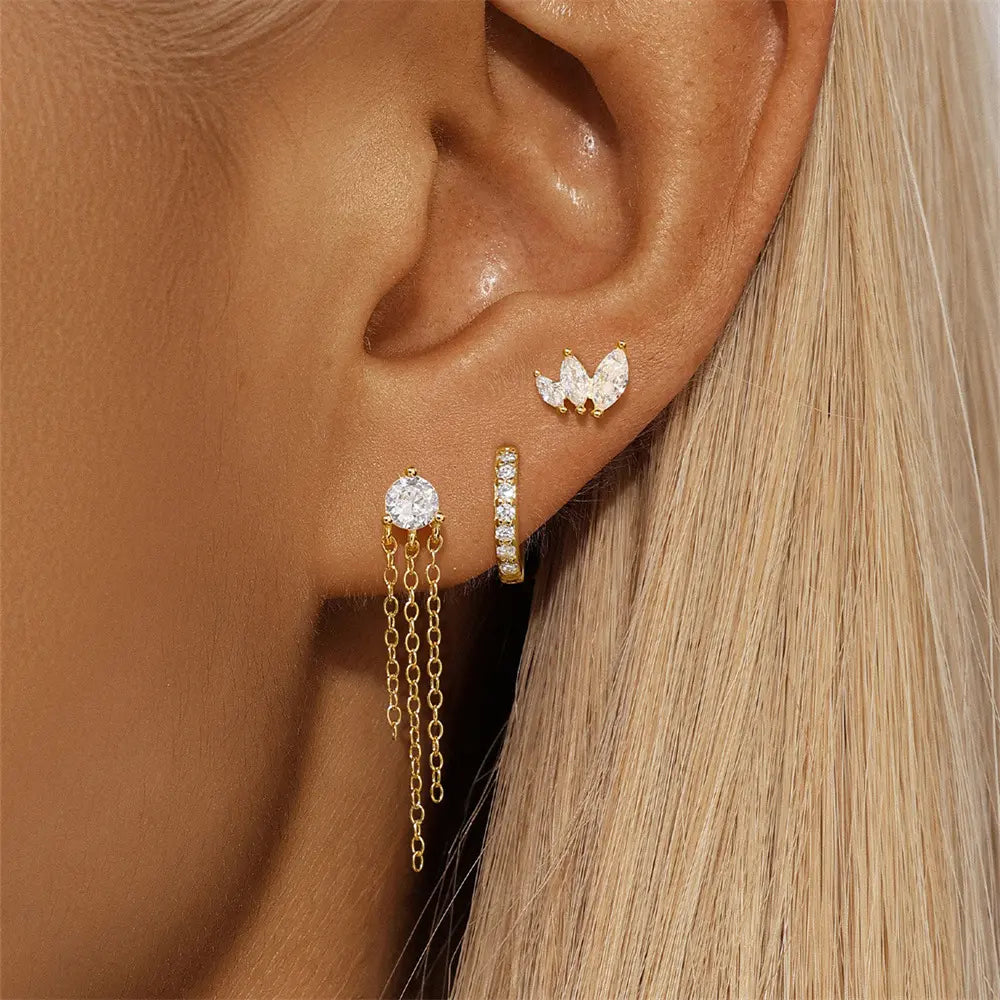 Model wearing a gold triple earring set, with marquise zircon studs, a chain-dangle zircon stud, and a small crystal hoop on her ear.