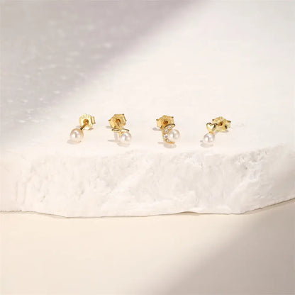 Set of gold stud earrings with pearl accents, featuring moon, star, heart, and round designs, displayed on a textured white background for an elegant presentation.