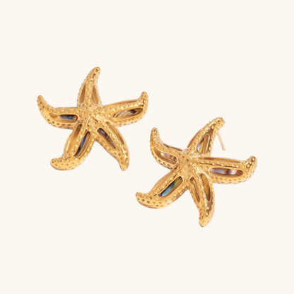 Close-up of scallop-shaped gold earrings with rainbow abalone shell detail